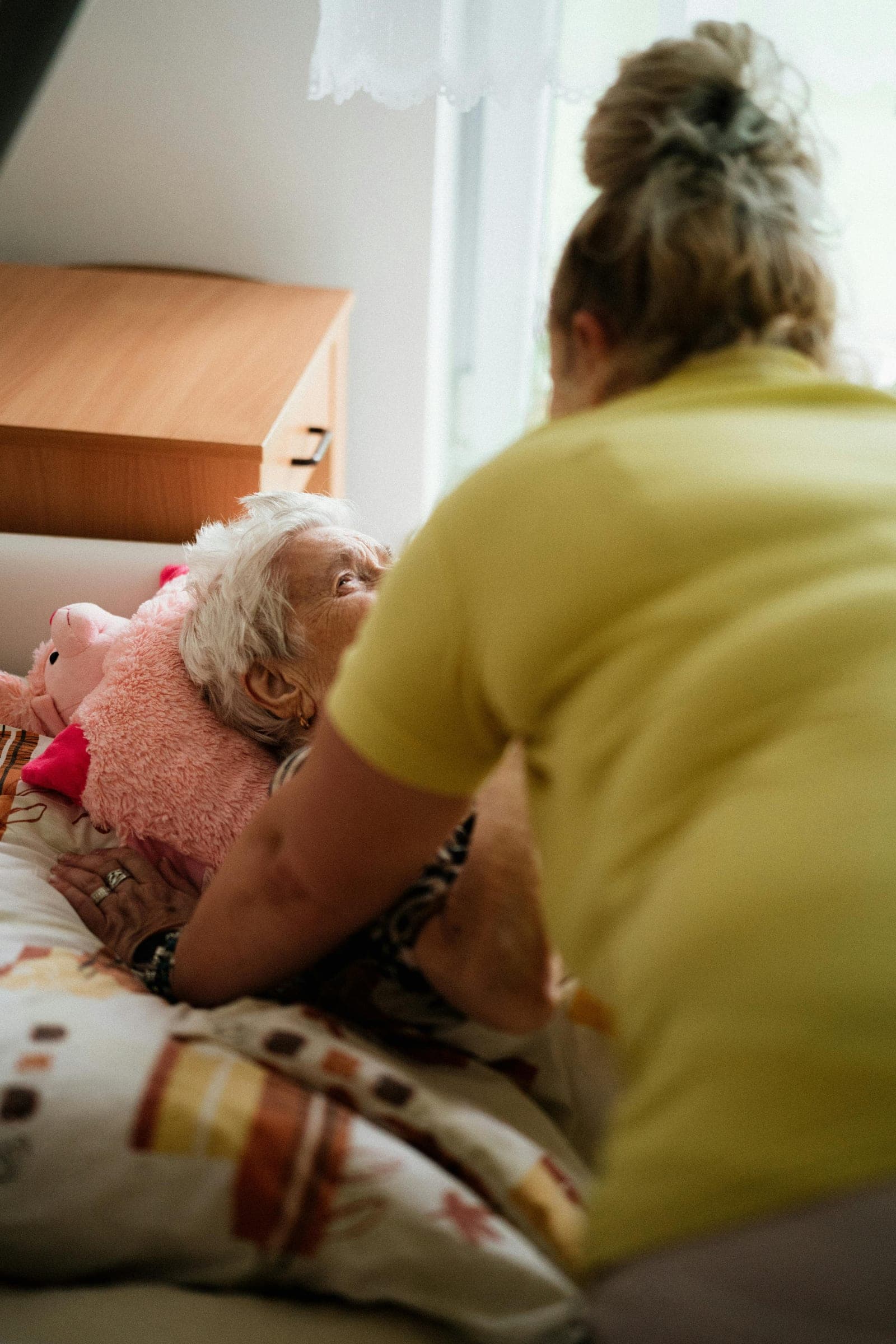 Cuidadora ajudando idosa na cama — cuidados de infecção urinária em Alzheimer