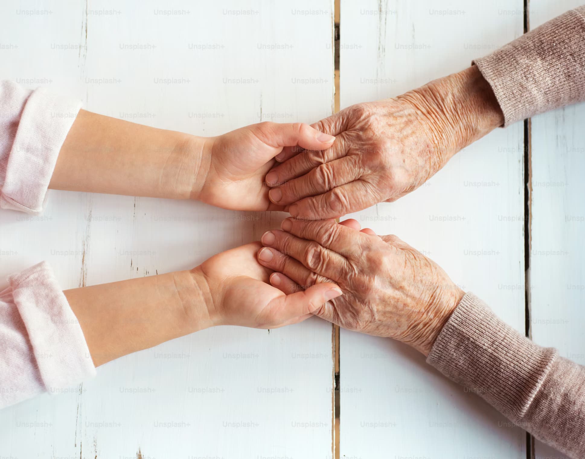 Mãos de pessoa jovem segurando carinhosamente as mãos de pessoa idosa, representando conexão e cuidado na demência